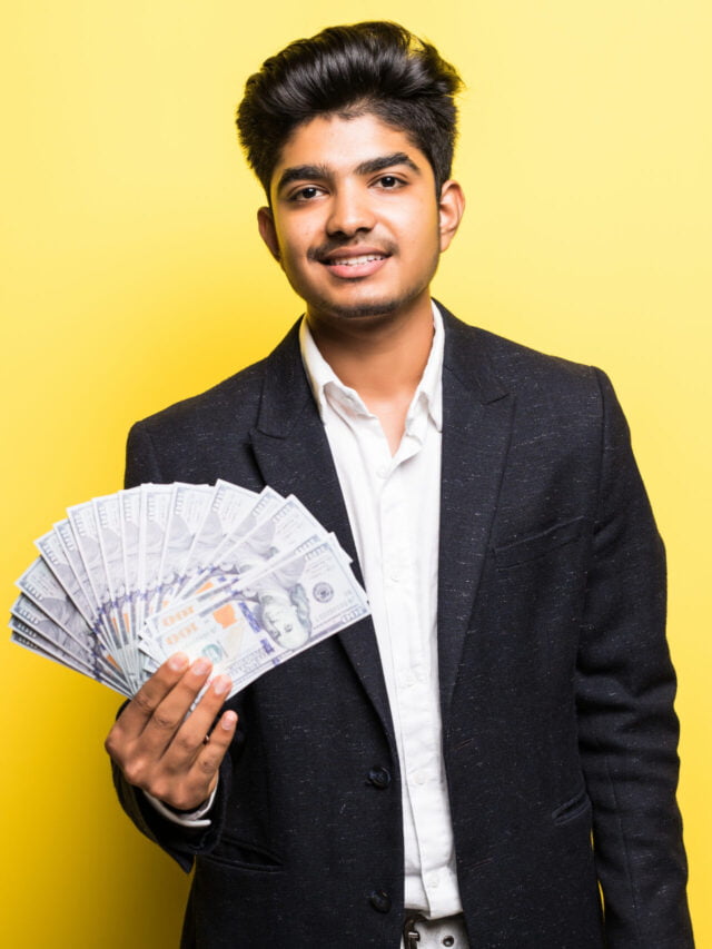Successful Indian entrepreneur with dollar banknotes in hand classical suit looking at camera with toothy smile while standing against yellow background